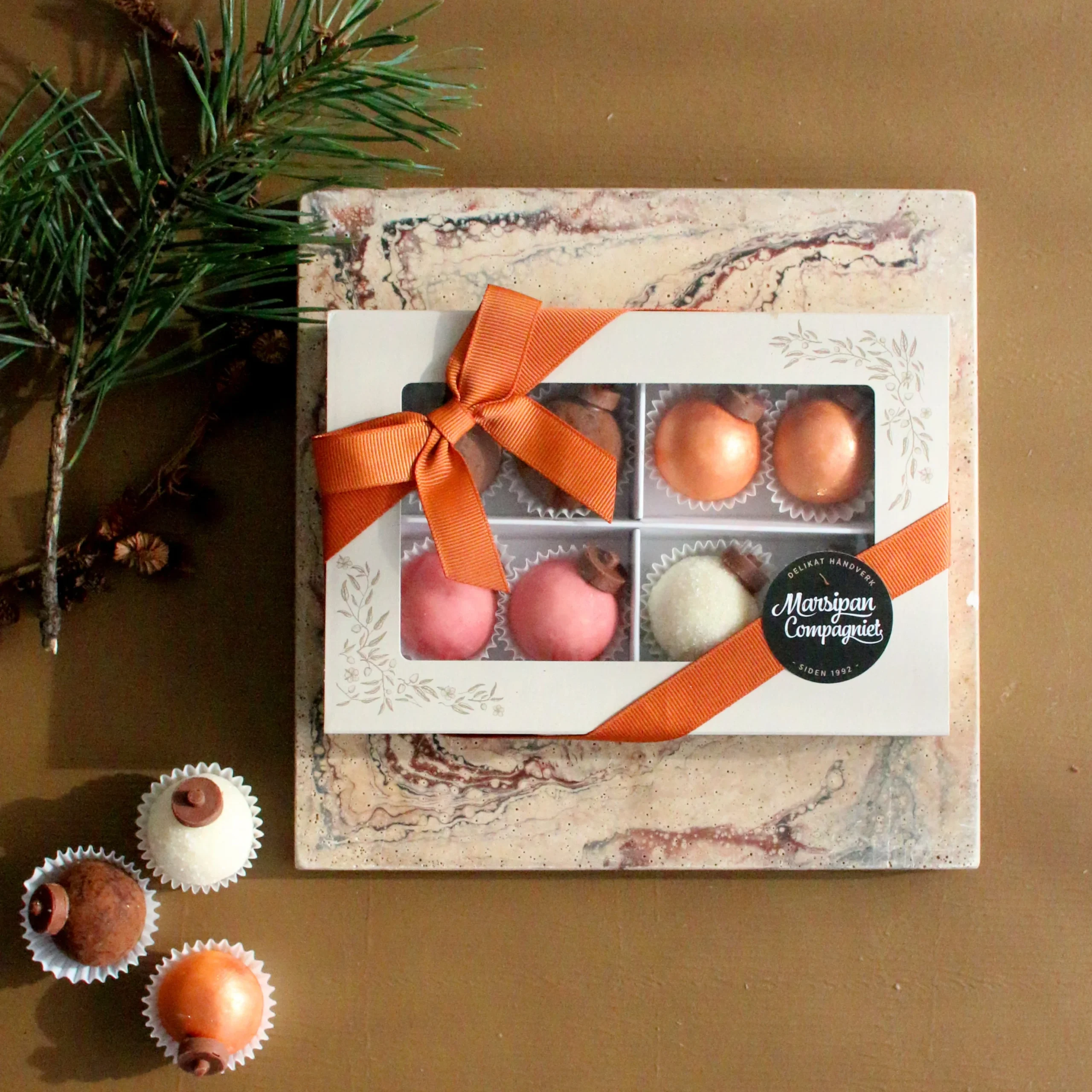 Søt liten eske for søt konfekt produsert av Moltzau Packaging for Marsipan Compagniets håndverkskonditori. Her med deres julekuler, pyntet med klistremerke og oransje bånd.